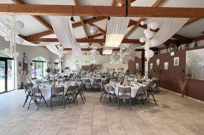 Salle de réception décorée avec des tables dressées, des fleurs et des voilages suspendus sous un plafond en bois.