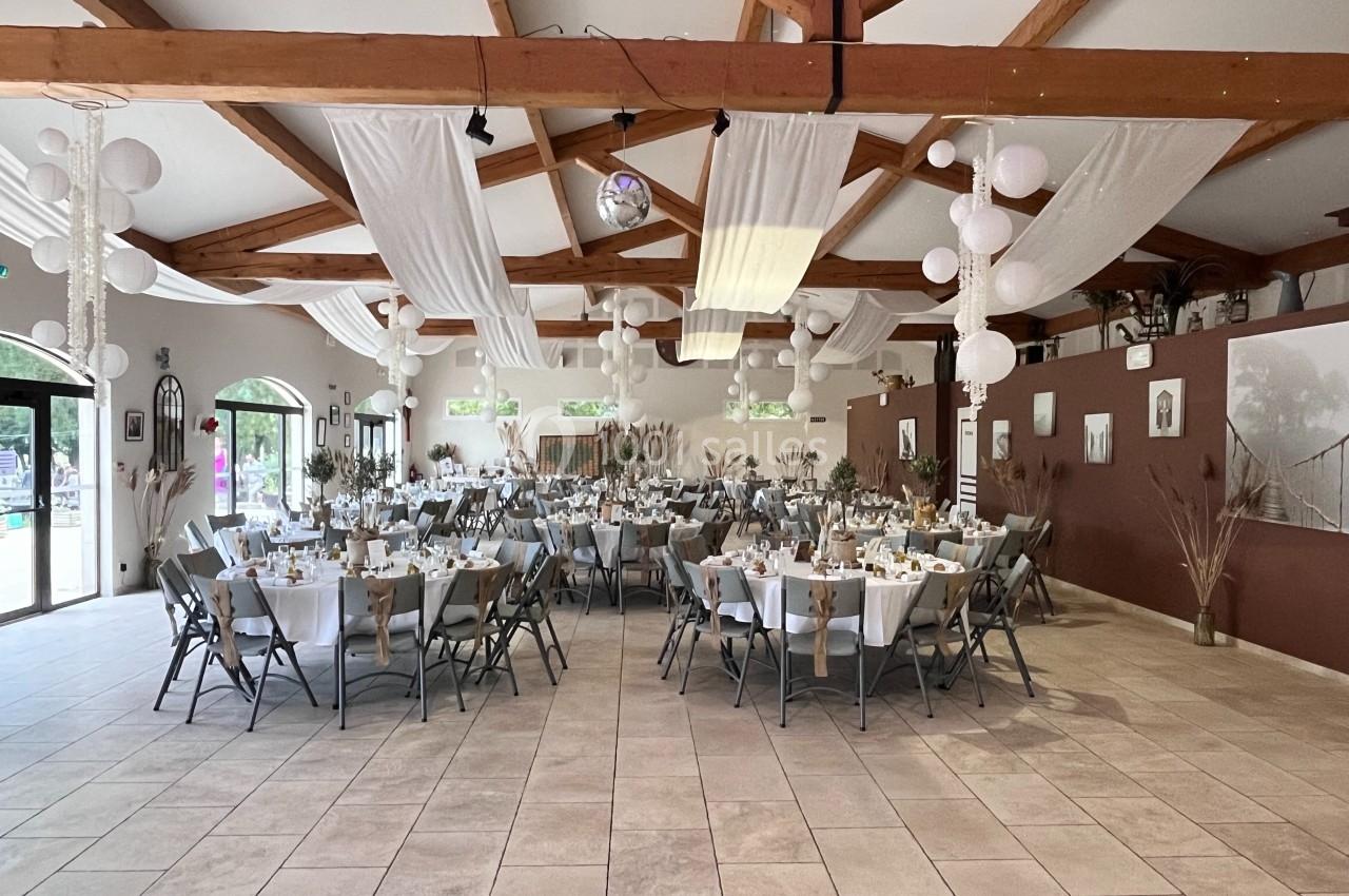 Salle de réception décorée avec des tables rondes dressées, des nappes blanches et des suspensions en tissu et lanternes.