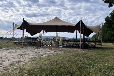 Salle de réception décorée avec des tables dressées, des fleurs et des voilages suspendus sous un plafond en bois.