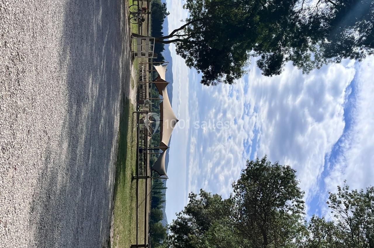 Chemin gravillonné bordé d'arbres menant à une structure couverte en toile dans un espace naturel.