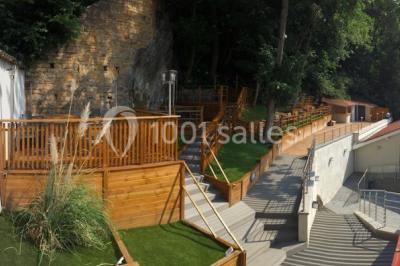 Tente blanche avec mobilier de jardin noir sur tapis rouge, installée devant une entrée vitrée d'un bâtiment beige.