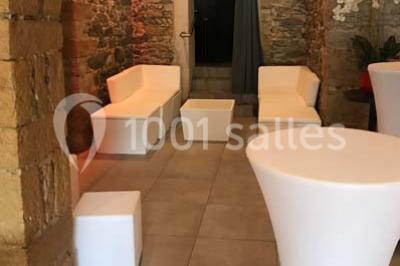 Tente blanche avec mobilier de jardin noir sur tapis rouge, installée devant une entrée vitrée d'un bâtiment beige.