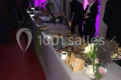 Tente blanche avec mobilier de jardin noir sur tapis rouge, installée devant une entrée vitrée d'un bâtiment beige.