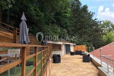 Tente blanche avec mobilier de jardin noir sur tapis rouge, installée devant une entrée vitrée d'un bâtiment beige.