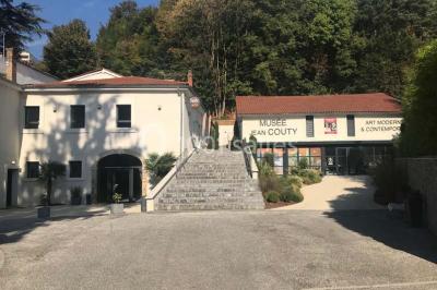 Tente blanche avec mobilier de jardin noir sur tapis rouge, installée devant une entrée vitrée d'un bâtiment beige.