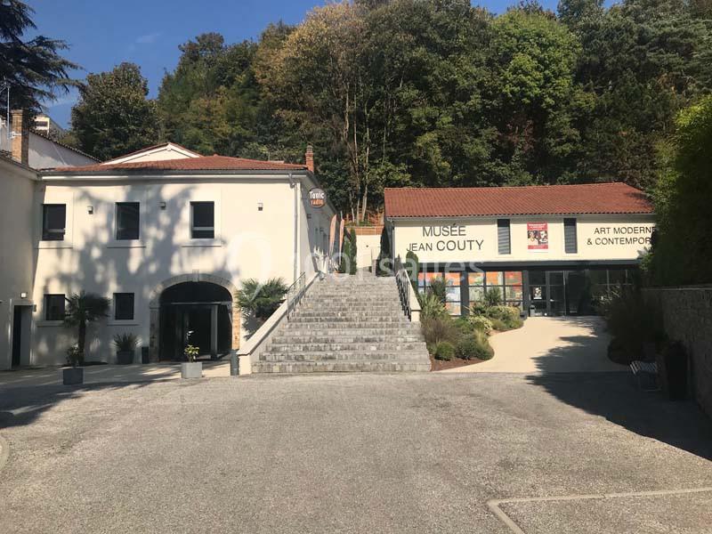 Escalier central menant à l'entrée du Musée Jean Couty, entouré de bâtiments et de végétation.