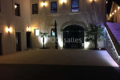 Tente blanche avec mobilier de jardin noir sur tapis rouge, installée devant une entrée vitrée d'un bâtiment beige.