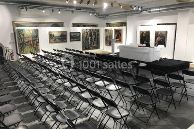 Cuisine professionnelle vide avec plans de travail en inox, évier, étagères ouvertes et réfrigérateurs en arrière-plan.