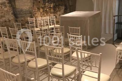 Cuisine professionnelle vide avec plans de travail en inox, évier, étagères ouvertes et réfrigérateurs en arrière-plan.