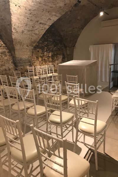 Chaises blanches disposées en rangées dans une salle voûtée en pierre avec une estrade couverte à l'avant.