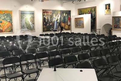 Cuisine professionnelle vide avec plans de travail en inox, évier, étagères ouvertes et réfrigérateurs en arrière-plan.