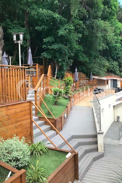 Escaliers et terrasses en bois entourés de végétation, menant à une structure moderne près d'une zone boisée.