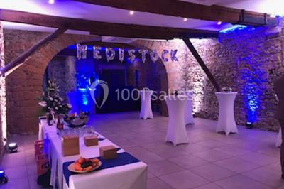 Cuisine professionnelle vide avec plans de travail en inox, évier, étagères ouvertes et réfrigérateurs en arrière-plan.