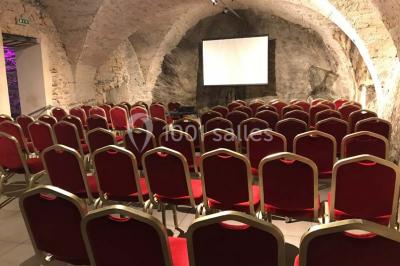 Cuisine professionnelle vide avec plans de travail en inox, évier, étagères ouvertes et réfrigérateurs en arrière-plan.