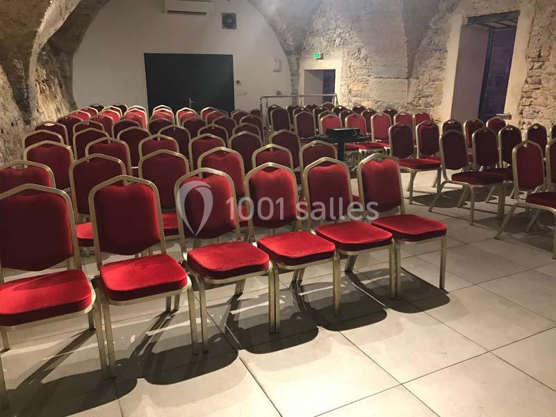 Salle voûtée avec des rangées de chaises rouges alignées, prête pour une réunion ou un événement.