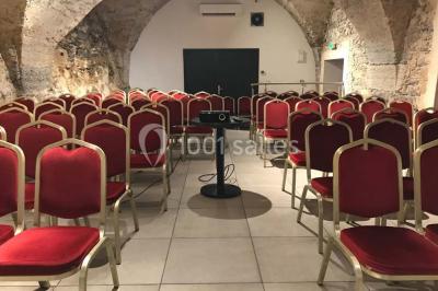 Cuisine professionnelle vide avec plans de travail en inox, évier, étagères ouvertes et réfrigérateurs en arrière-plan.