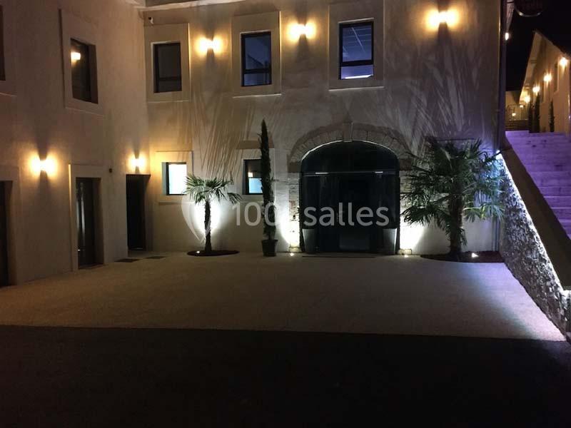 Façade d'un bâtiment éclairé la nuit, avec des palmiers et une entrée principale en arc de pierre.