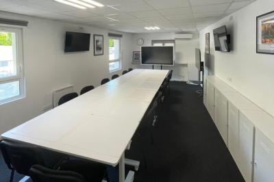 Cuisine professionnelle vide avec plans de travail en inox, évier, étagères ouvertes et réfrigérateurs en arrière-plan.