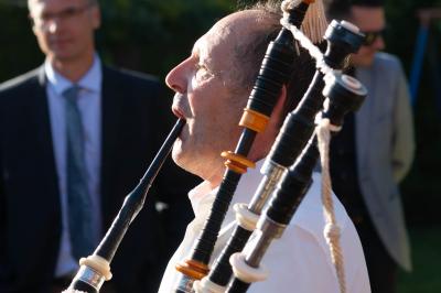 Un couple de mariés ému écoute un joueur de cornemuse, entouré d'invités applaudissant dans une salle lumineuse.