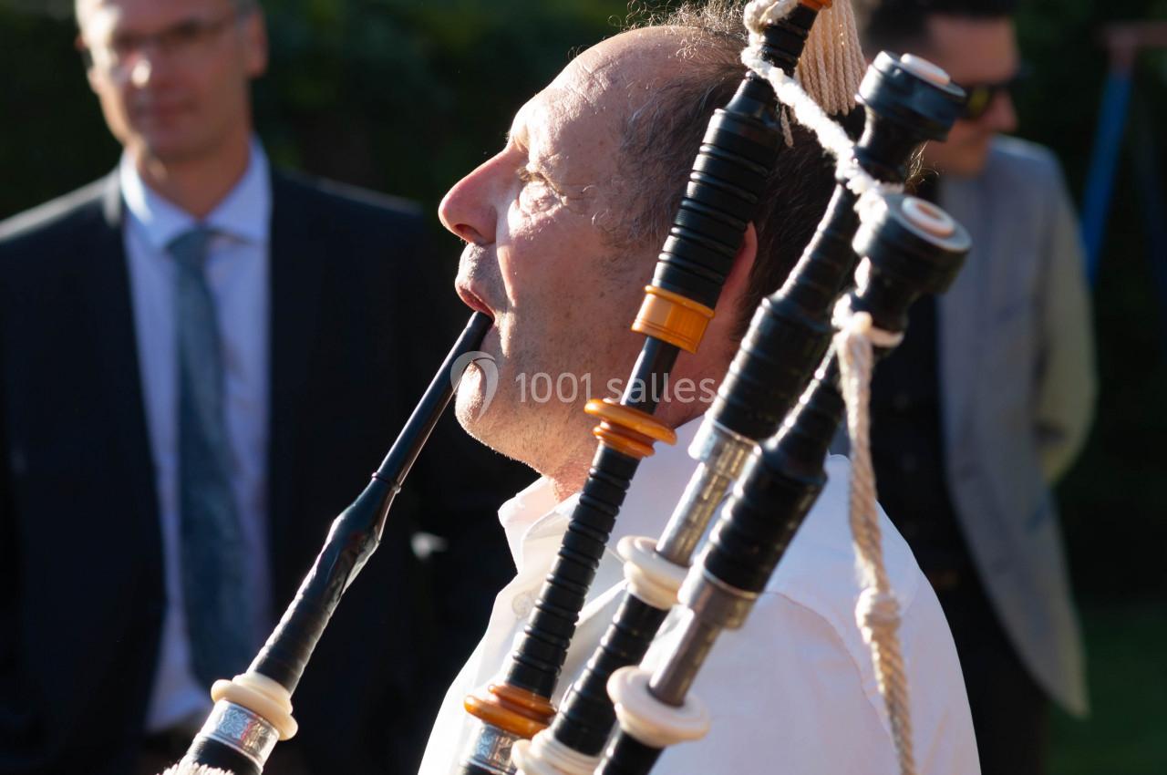 Homme jouant de la cornemuse en extérieur, avec des spectateurs en arrière-plan.