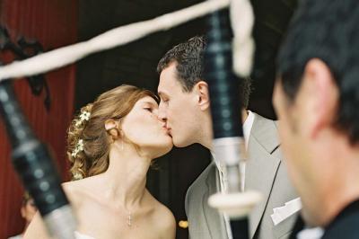 Un couple de mariés ému écoute un joueur de cornemuse, entouré d'invités applaudissant dans une salle lumineuse.