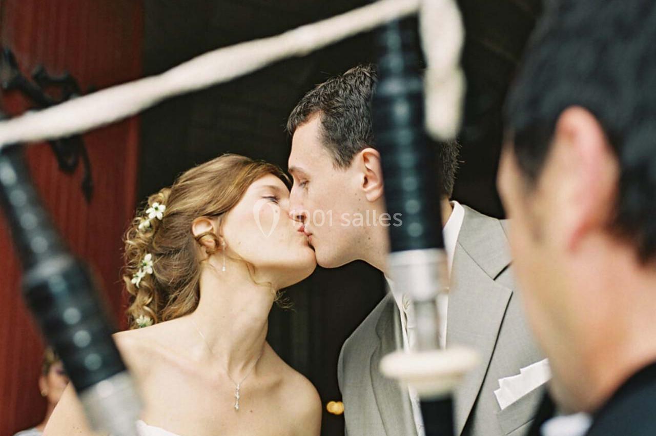 Un couple s'embrasse lors d'une cérémonie, avec un joueur de cornemuse visible au premier plan.