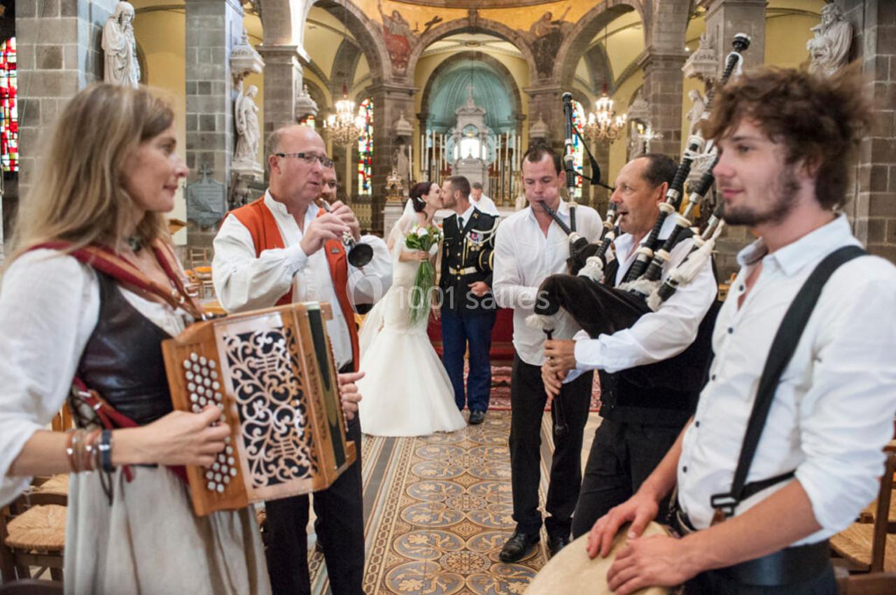Un groupe de musiciens joue dans une église pendant un mariage, avec les mariés en arrière-plan.