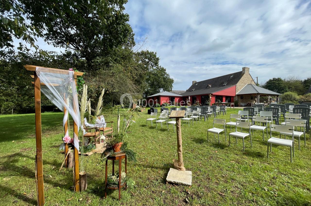 Espace extérieur aménagé pour une cérémonie, avec arche décorée, chaises alignées et bâtiment en arrière-plan.