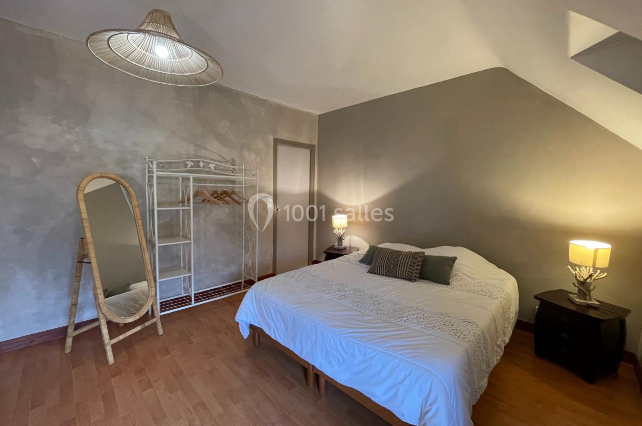 Chambre lumineuse avec lit double, miroir sur pied, étagère en métal et lampes de chevet sur tables noires.