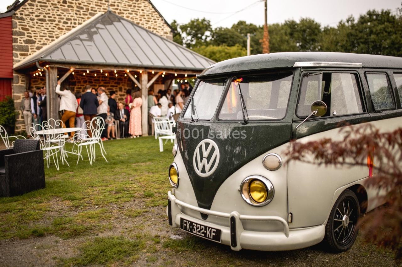 Un van Volkswagen vintage garé devant une réception en plein air près d'un bâtiment en pierre.