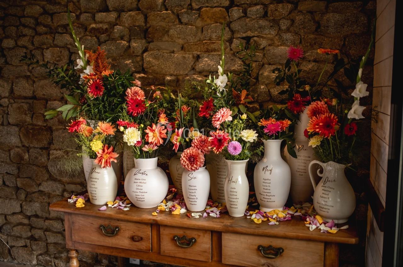 Vases en céramique blanche remplis de fleurs colorées, disposés sur une table en bois devant un mur en pierre.