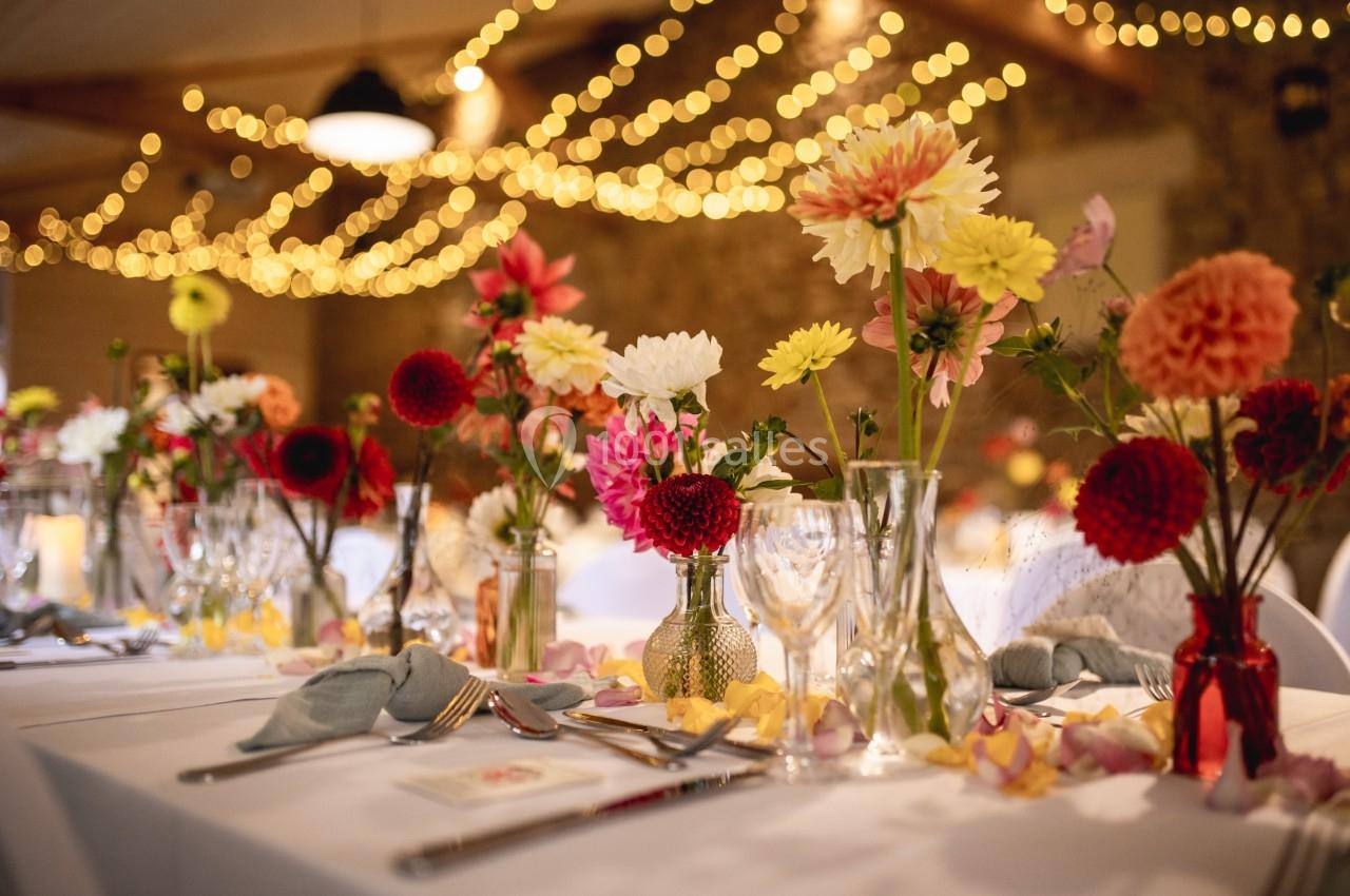 Tables décorées de bouquets colorés et de pétales, éclairées par des guirlandes lumineuses dans une salle chaleureuse.