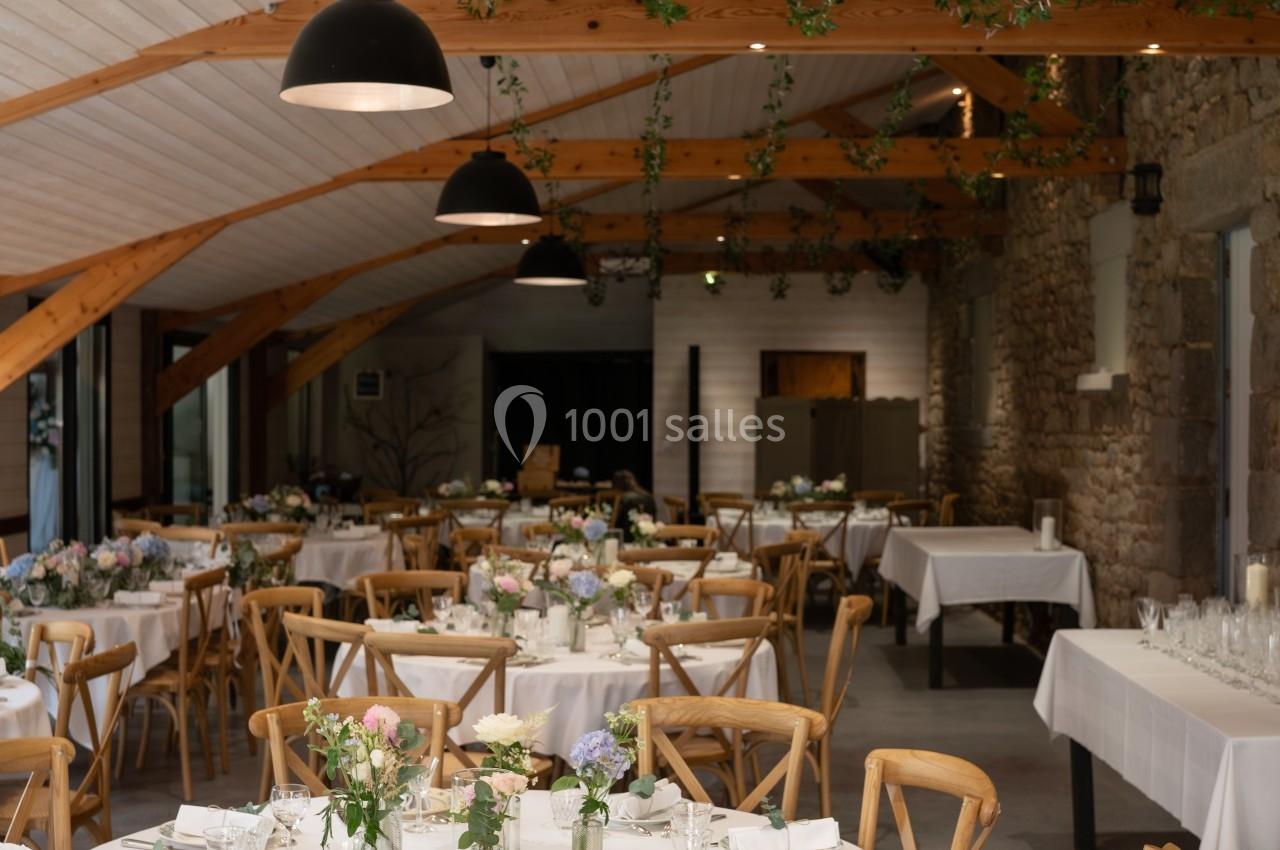 Salle de réception lumineuse avec tables rondes décorées de nappes blanches, fleurs et chaises en bois clair.