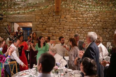Un couple de mariés ému écoute un joueur de cornemuse, entouré d'invités applaudissant dans une salle lumineuse.