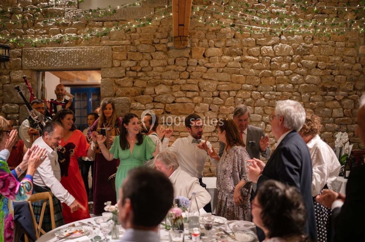 Des invités dansent et discutent lors d'une réception dans une salle en pierre décorée de guirlandes lumineuses.