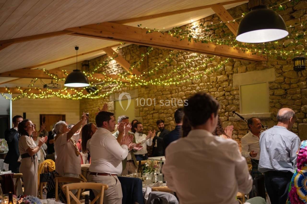 Des invités applaudissent dans une salle décorée de guirlandes lumineuses et de murs en pierre apparente.