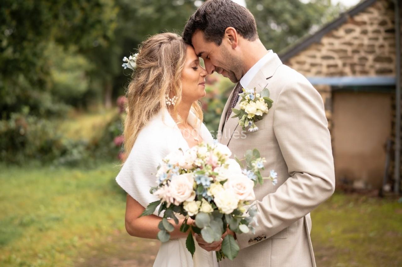 Un couple de mariés s'enlace tendrement dans un jardin, tenant un bouquet de fleurs pastel.