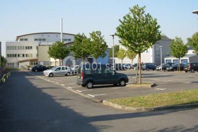 Parking extérieur avec quelques voitures stationnées, entouré de bâtiments modernes et d'arbres alignés.