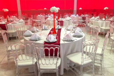 Salle de réception décorée avec des tables rondes, nappes blanches, chaises transparentes et centres de table fleuris.