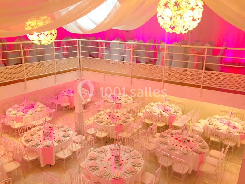 Salle de réception décorée avec des tables rondes dressées, éclairage rose et lustres suspendus.
