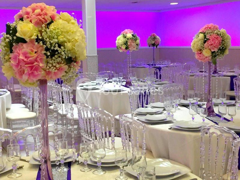 Salle de réception décorée avec des tables dressées et des centres de table fleuris dans des tons pastel.