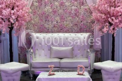 Salle de réception décorée avec des tables rondes, nappes blanches, chaises transparentes et centres de table fleuris.