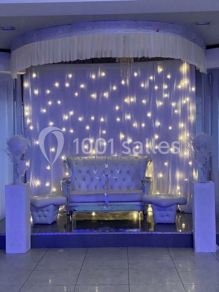 Canapé blanc capitonné devant un rideau illuminé de guirlandes lumineuses, encadré par deux colonnes décoratives.