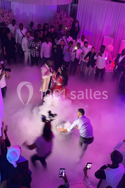 Un couple danse au centre d'une salle entourée d'invités, avec un sol couvert de fumée et des lumières colorées.