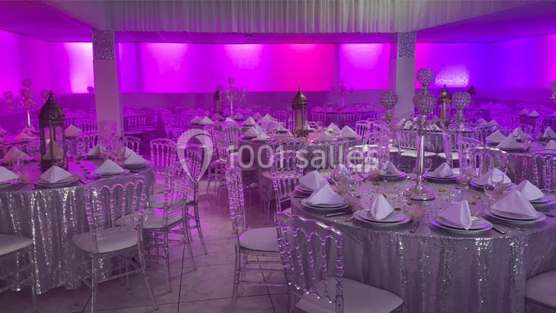 Salle de réception décorée avec des tables rondes couvertes de nappes scintillantes et éclairage rose tamisé.