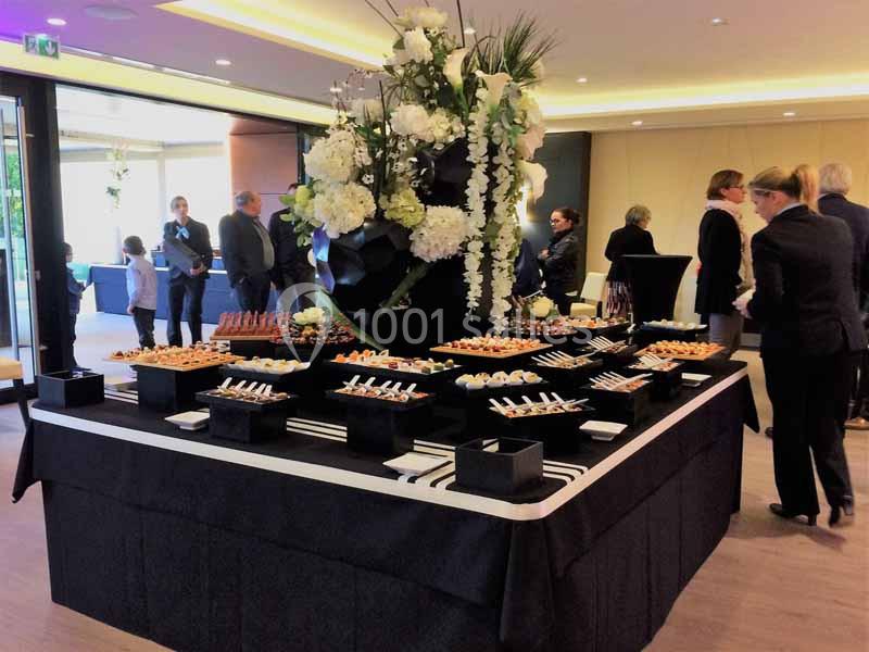 Table de buffet élégante avec des fleurs blanches en centre de table, entourée de convives dans une salle lumineuse.