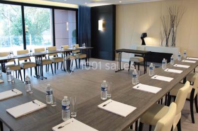 Espace lounge avec canapés blancs, tables basses et vue sur une terrasse arborée avec des tables hautes.