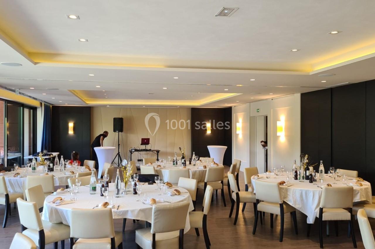 Salle de réception lumineuse avec tables rondes dressées, chaises beige clair et décoration sobre.