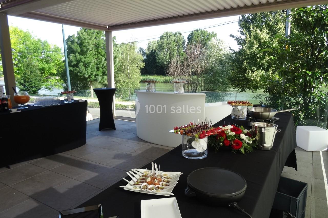Buffet extérieur avec tables noires garnies de fleurs, amuse-bouches et boissons, sous une pergola près d'un jardin.