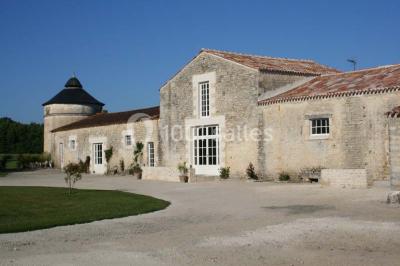 Miniature Location salle Benon (Charente-Maritime) - Abbaye de la Grâce-Dieu #2 Salon lumineux avec murs blancs, plafond voûté, cheminée centrale, meubles anciens et canapés gris.